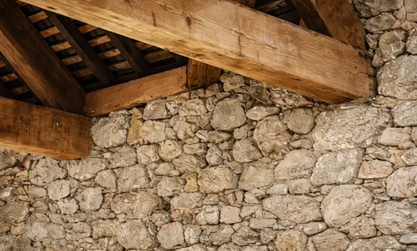 Détails d'un mur en pierre avec deux poutres en bois dont les abouts sont encastrées dans le mur.