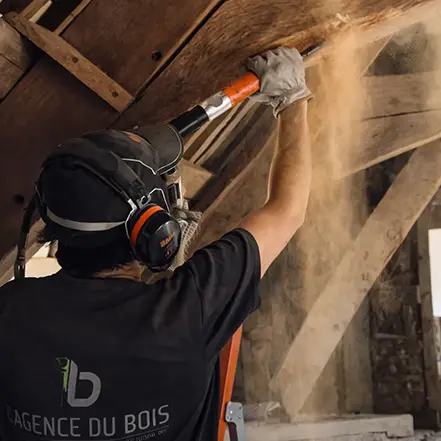 image secteurs d'intervention : bûchage de l'aubier sur une poutre en bois à l'aide d'un ciseau électrique.